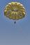 Senior white woman is parasailing.She is flying under yellow parachute in blue sky, smiling and opening her arms.