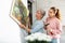 Senior woman with adult daughter hanging picture on wall at home