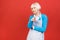 Senior woman in apron standing isolated on red background. She is a good housewife. She likes to cook tasty food