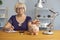 Senior woman calculates income and throws coins into a piggy bank while sitting at a table.