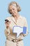 Senior woman with cell phone holding fake dislike button against blue background