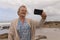 Senior woman clicking photos with mobile phone at beach