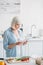 senior woman with digital tablet standing at counter with fresh vegetables