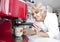 Senior woman dispensing coffee from machine at kitchen counter