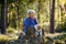 A senior woman with dog on a walk outdoors in forest, resting.