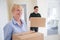 Senior Woman Downsizing In Retirement Carrying Boxes Into New Home On Moving Day With Removal Man Helping