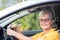 Senior woman driving a car in the city. Portrait of attractive elderly woman looking out of the window and smiling