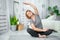 Senior woman exercising while sitting in lotus position. Active mature woman doing stretching exercise in living room at home.