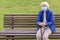 Senior woman in face mask with cane in hands sitting on bench in park