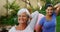 Senior woman with female trainer doing stretching exercise in garden 4k