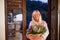 Senior woman with flowers in basket standing outdoors on terrace.