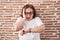 Senior woman with glasses standing over bricks wall looking at the watch time worried, afraid of getting late