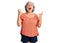 Senior woman with gray hair wearing orange tshirt crazy and mad shouting and yelling with aggressive expression and arms raised