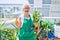 Senior woman with grey hair wearing gloves and gardener apron gardening the plants at home doing thumbs up gesture