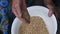 Senior woman hand pouring raw buckwheat grains into old white enamel bowl