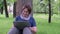 Senior woman having online call while sitting on the grass in city park.