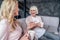 Senior woman and her attractive daughter spending time together at home. Sitting on sofa and drinking tea together. Happy Mothers