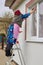 Senior woman with a ladder washes the window,pensioner stands on a ladder and washes the window