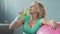 Senior woman leaning on fitness ball, drinking water after workout, hydration