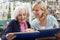 Senior Woman Looks At Photo Album With Mature Female Neighbor