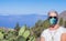 Senior woman in medical mask traveling in mountain landscape in Tenerife, horizon over the sea - new normal life concept in summer