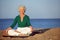 Senior woman meditating on sandy beach