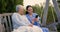 Senior woman, nurse and outdoor with phone, laugh and funny video on swing chair, relax and reading chat. Caregiver