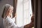 Senior Woman Opening Bedroom Curtains And Looking Out Of Window