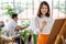 Senior woman painting image in studio with husband blur in background