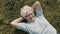 Senior woman, pensioner lying on the grass with hands under her head in the garden overhead close up shot