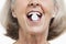 Senior woman with a pill between her teeth against white background