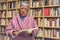 Senior woman reading a book at home. Serious expression. A blurred library is in the background.