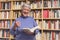 Senior woman reading a book at home. Thumbs up, motivated expression. A blurred library is in the background.