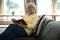 Senior woman reading book on sofa in living room