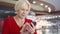 Senior woman in shopping mall smiling. Using her smartphone, browsing, reading news, chatting