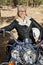 Senior woman sits on motorbike with forest in background