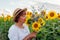 Senior woman smells bouquet of yellow sunflowers in summer field at sunset. Middle-aged woman admires blooms