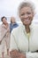 Senior Woman Stands In Fleece Jacket With Friends On Beach