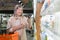 Senior woman in a supermarket in the dairy department, chooses food near the refrigerator with a phone