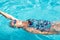 Senior woman swims backstroke in transparent outdoor pool water. Healthy activity and lifestyle for retiree