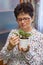 Senior woman taking care of plants at home, removing dead leaves from a plant, vertical