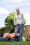 Senior Woman Using Electric Lawn Mower To Cut Grass At Home