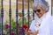 Senior woman using mobile phone while standing in the garden. Portrait of a beautiful elderly woman reading online messages