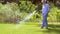 Senior woman watering lawn by hose at garden