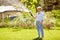 Senior woman watering lawn by hose at garden