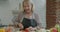 Senior woman wearing apron cutting tomato making salad preparing lunch at home in kitchen