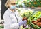 Senior woman wearing face mask and rubber gloves selects peppers and other vegetables  in a supermarket -safe and healthy