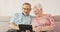 The seniors are relaxing on the sofa in their cosy living room. Tablet in the
