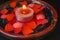 Sensational decorative aroma candle with red flower petals around on red and black plate.