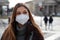 Sense of bewilderment. Close up of young woman in winter clothes walking in street wearing protective mask FFP2 KN95. Girl with